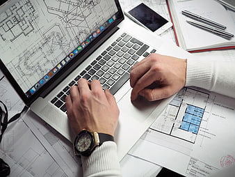 Architect working on laptop with blueprints and smartphone