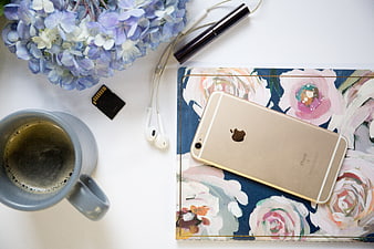 Flat lay of gold smartphone, coffee, and flowers on desk