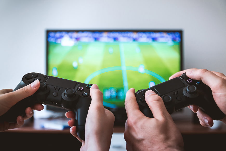 Hands holding game controllers playing soccer video game on TV