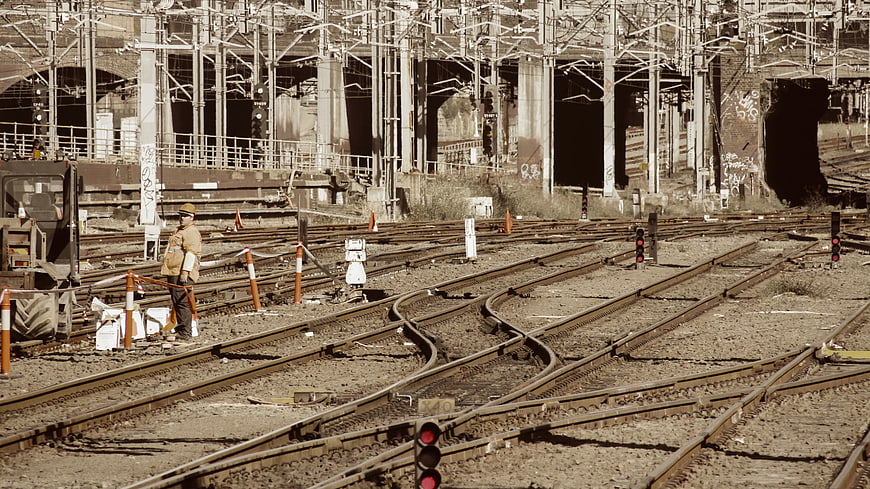 Railway Worker Standing Near Tracks in Industrial Yard