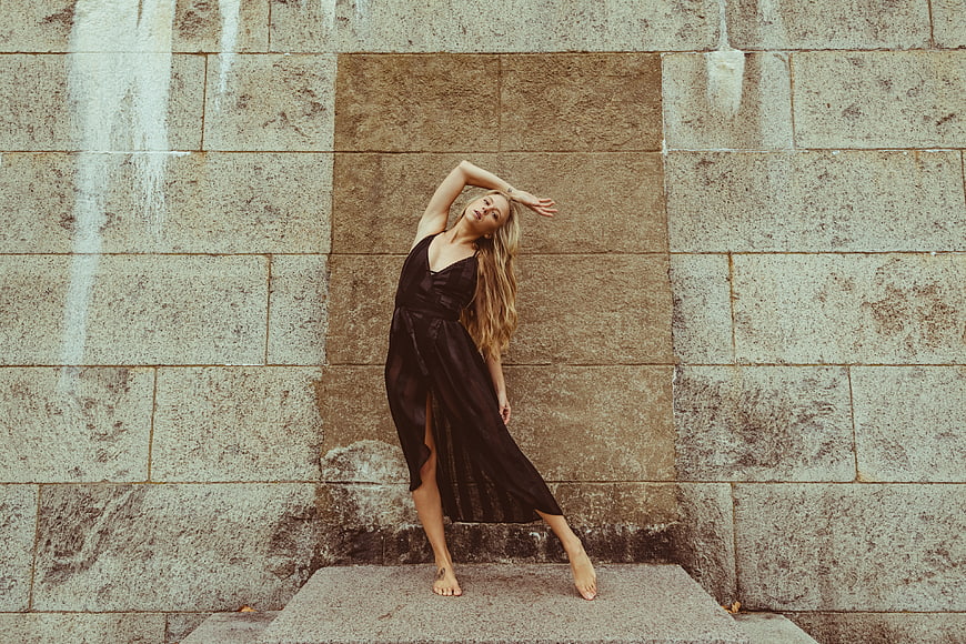 Blonde woman in black dress posing against stone wall