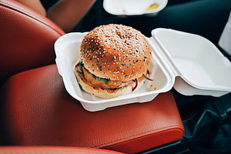 Delicious burger in takeout container on red car seat