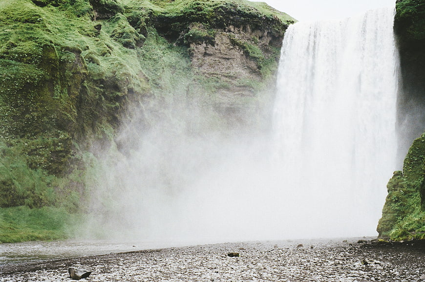 Majestic waterfall cascading into misty river with mossy cliffs