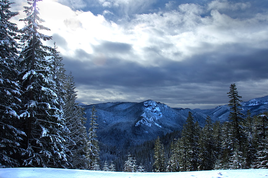 Snowy Mountain Landscape with Pine Trees and Dramatic Clouds