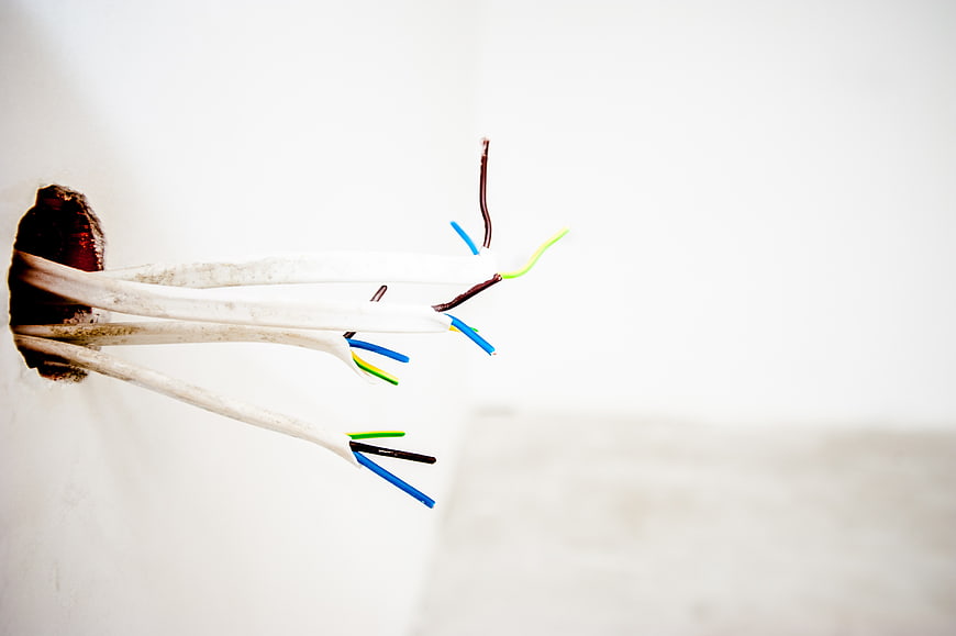 Exposed electrical wires protruding from a white wall