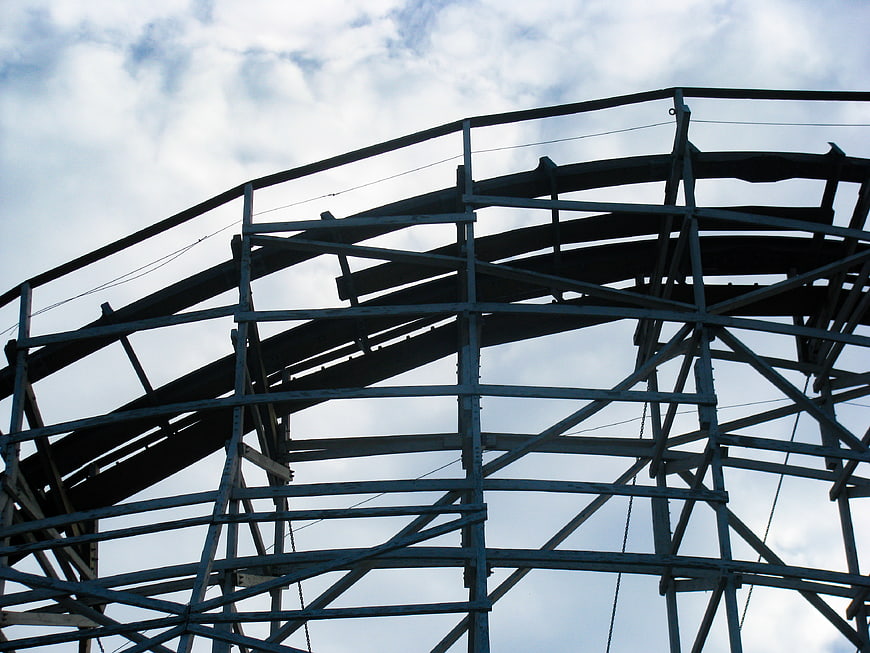 Low angle view of wooden roller coaster tracks against cloudy sky