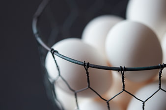 Close-up of white eggs in a wire basket on dark background
