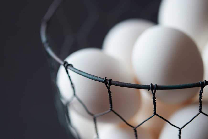 Close-up of white eggs in a wire basket on dark background