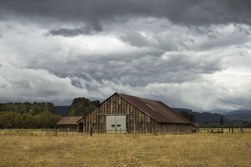 Weathered wooden barn in rural field under dramatic storm clouds