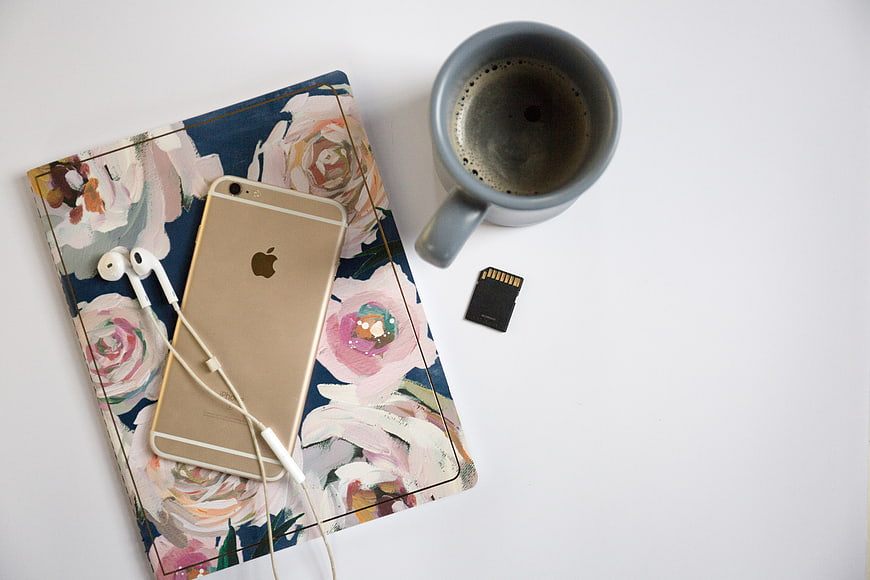 Flat lay of smartphone, headphones, coffee, and floral notebook