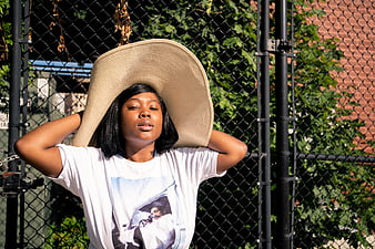 Woman in oversized hat relaxing against chain link fence