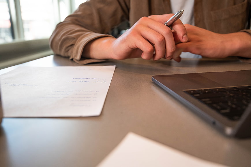 Close-up of hands holding pen at office desk with laptop