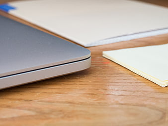 Close-up of laptop corner and notepad on wooden desk