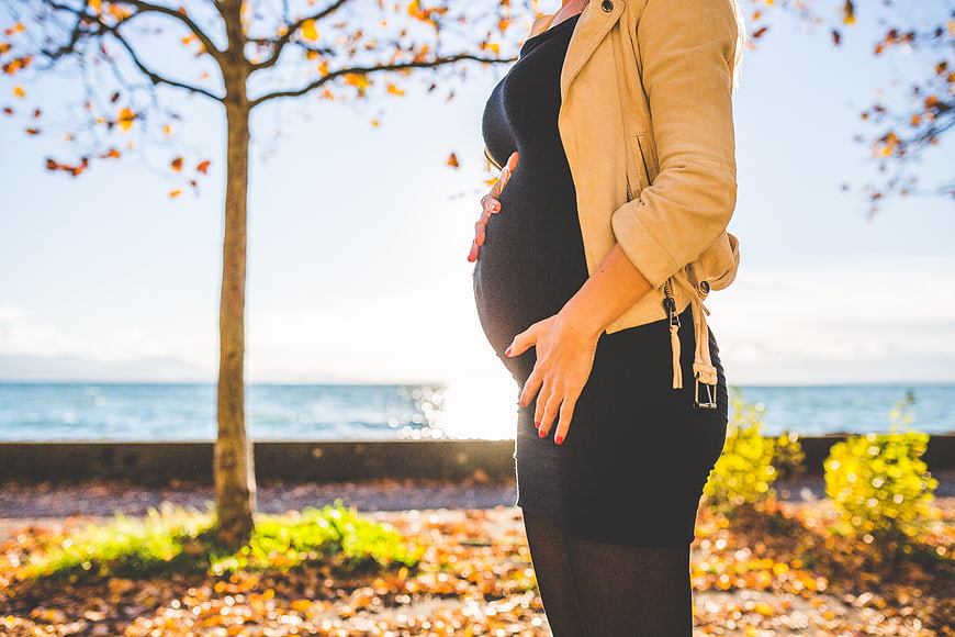Pregnant woman holding belly in autumn park by sea
