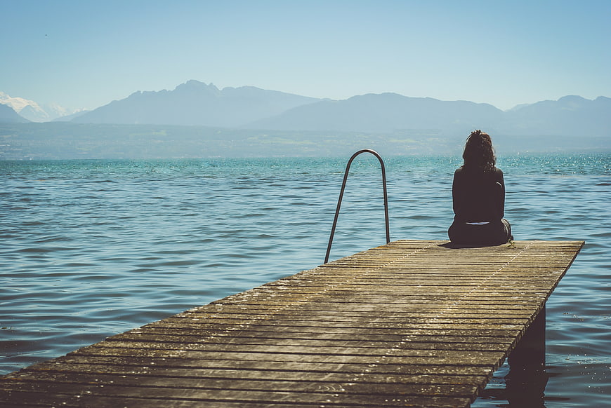 Woman sitting on wooden pier overlooking lake and mountains