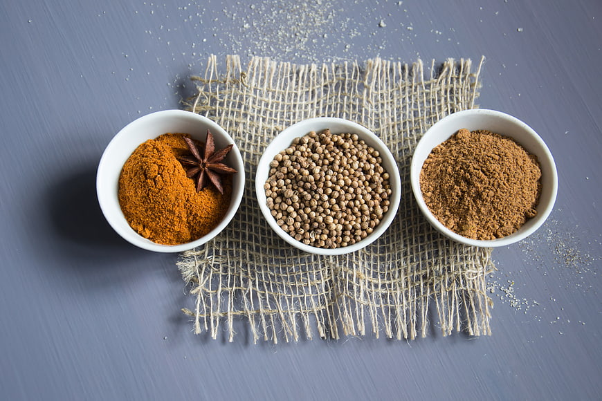 Top view of turmeric, coriander, and nutmeg in white bowls