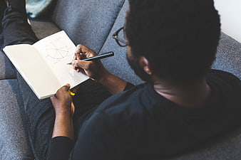 Man sketching design in notebook on sofa