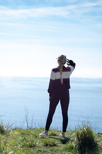 Woman with braided hair looking out at the ocean from a grassy cliff