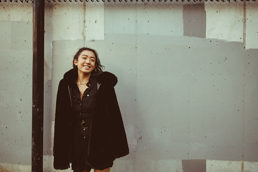 Happy Asian Woman in Black Coat Against Concrete Wall