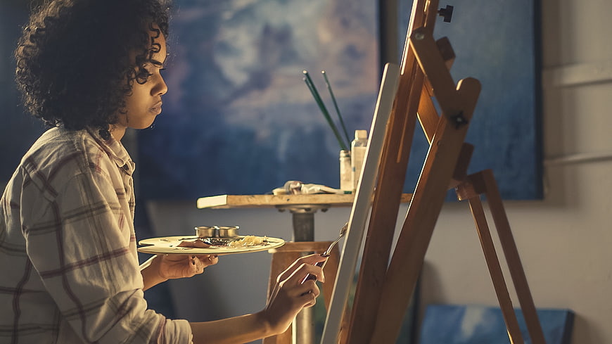 Young woman artist painting on canvas in studio