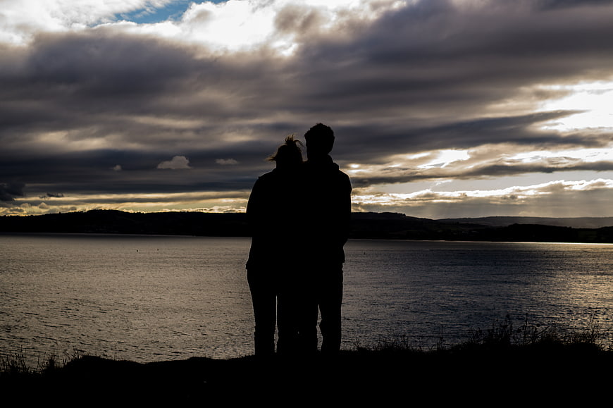 Silhouette of a couple standing by a lake at sunset