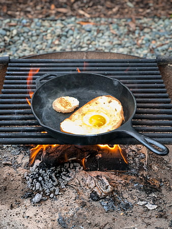 Camping breakfast with eggs and toast in cast iron skillet over fire