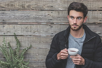 Young Man Holding Coffee Cup Against Wooden Wall