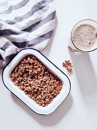 Overhead view of granola in white bowl with milk and striped cloth