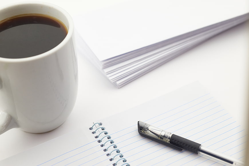 White coffee mug, pen, and notebook on white desk