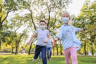 Children wearing face masks running in a sunny park
