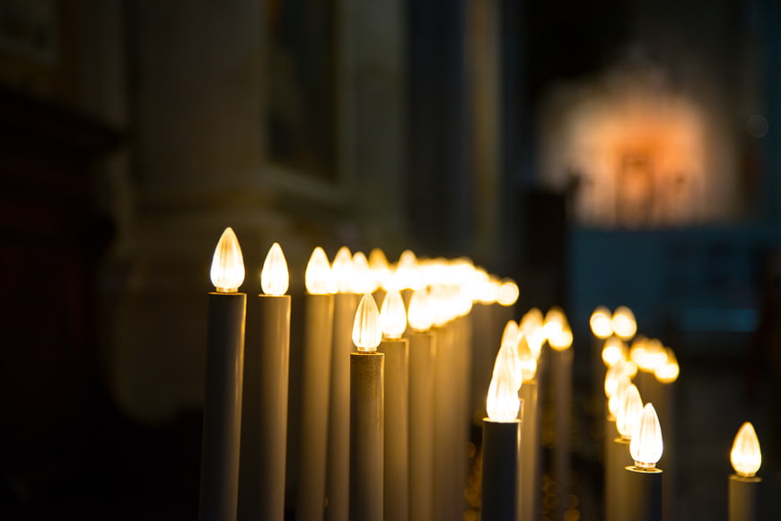 Rows of lit electric candles in a dimly lit church interior