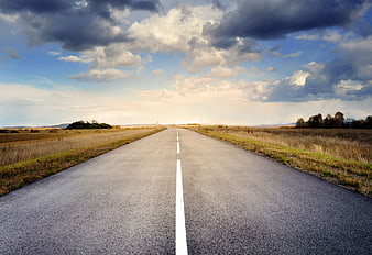 Straight asphalt road stretching to horizon under dramatic cloudy sky