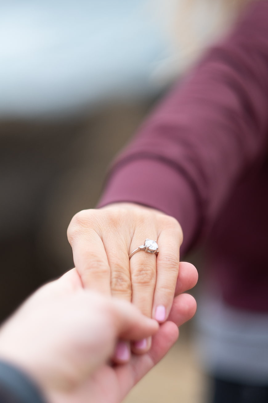 Close-up of engagement ring on woman's hand held by partner