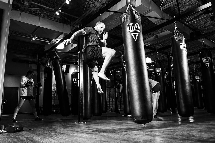 Athletic man performing high kick on heavy bag in boxing gym