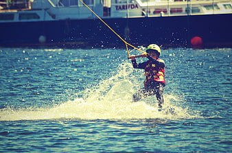 Child waterskiing with helmet and life jacket on sunny day
