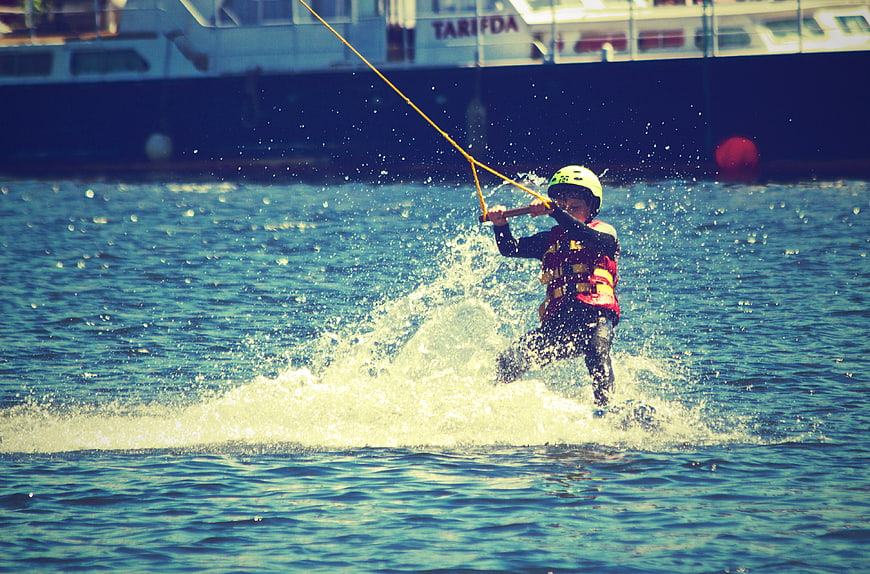 Child waterskiing with helmet and life jacket on sunny day