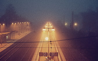 Foggy train station tracks illuminated by warm streetlights at night
