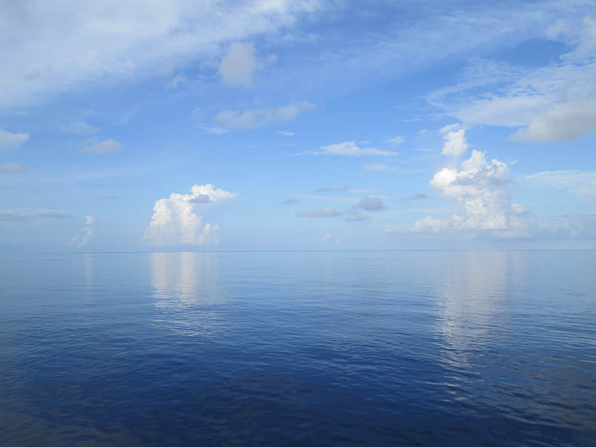 Serene Ocean Horizon with Fluffy White Clouds and Blue Sky