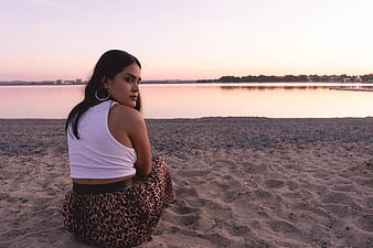 Woman Sitting on Sandy Beach at Sunset Looking Back