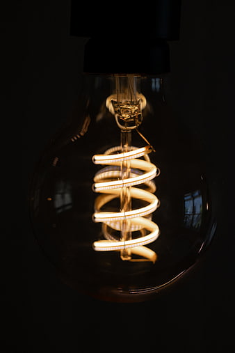 Illuminated spiral CFL light bulb against dark background