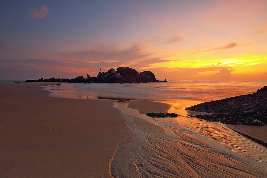 Serene Beach Sunset with Rocky Outcrop and Golden Sky
