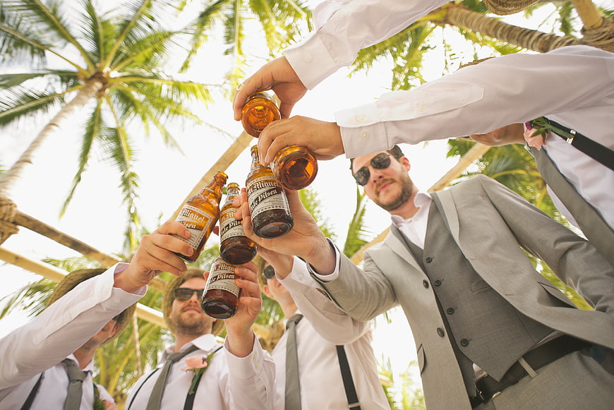 Groomsmen toasting with beer bottles under palm trees