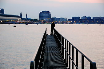 Silhouette of person standing on pier at dusk with city skyline