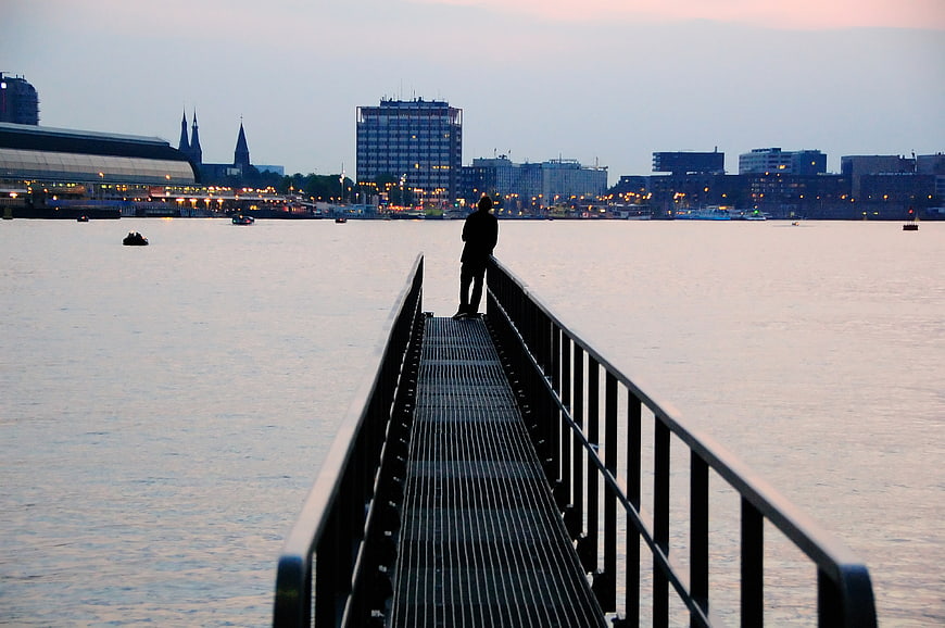 Silhouette of person standing on pier at dusk with city skyline