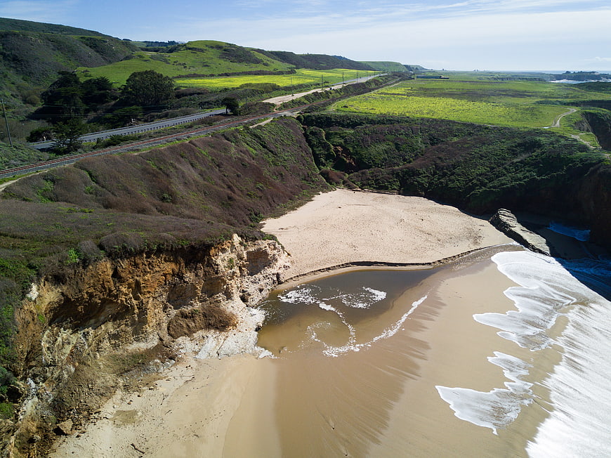 Aerial view of coastal cliffs, sandy beach, and green hills