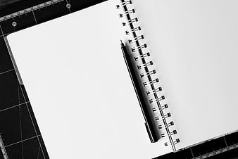 Black pen on blank spiral notebook with cutting mat background