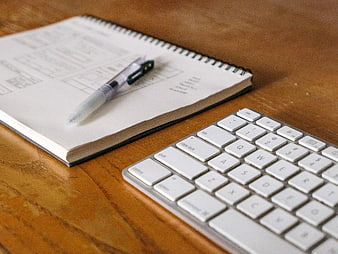 Minimalist workspace with notebook, pen, and keyboard on wooden desk