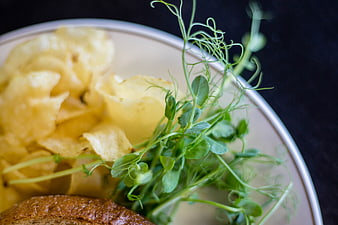Close-up of potato chips, pea shoots, and bread on a plate