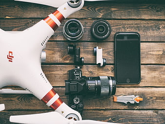 Flat lay of DJI drone, DSLR camera, lenses, and smartphone on wood