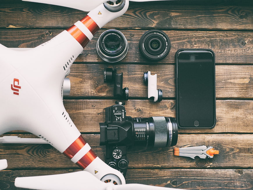 Flat lay of DJI drone, DSLR camera, lenses, and smartphone on wood